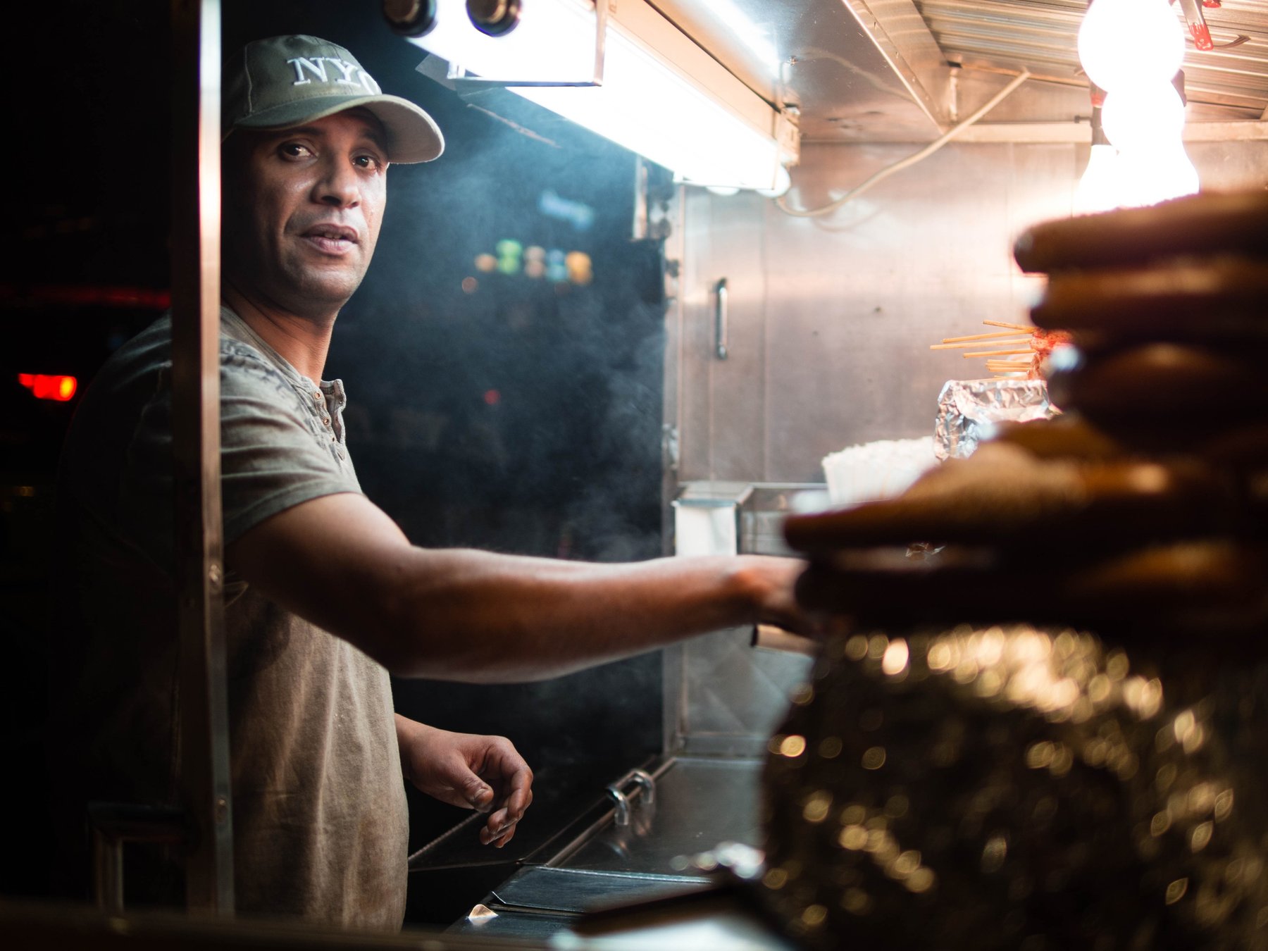 A man working beside a steaming stack of food at a market stall.