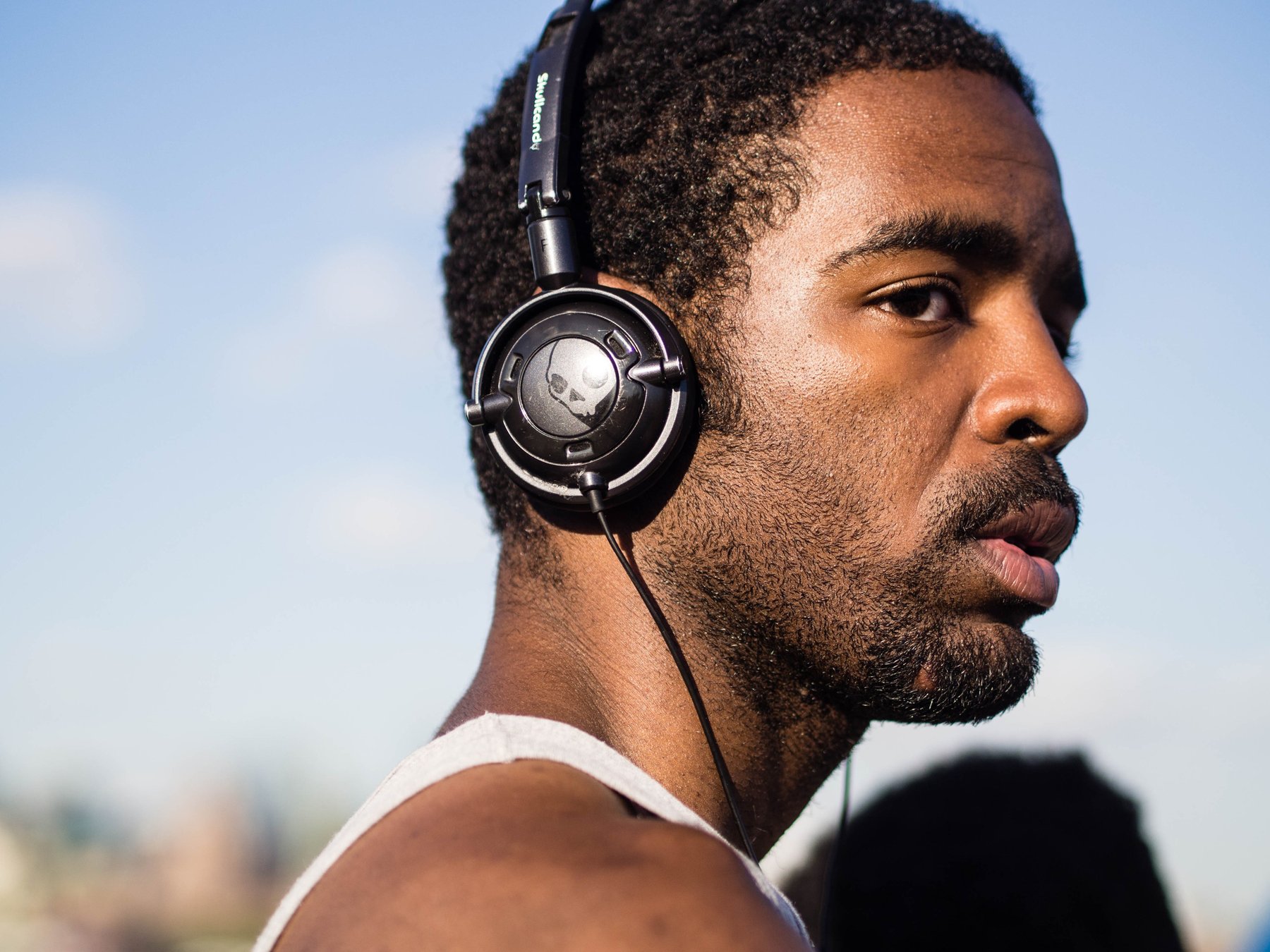 A close portrait of a man wearing headphones under a blue sky.