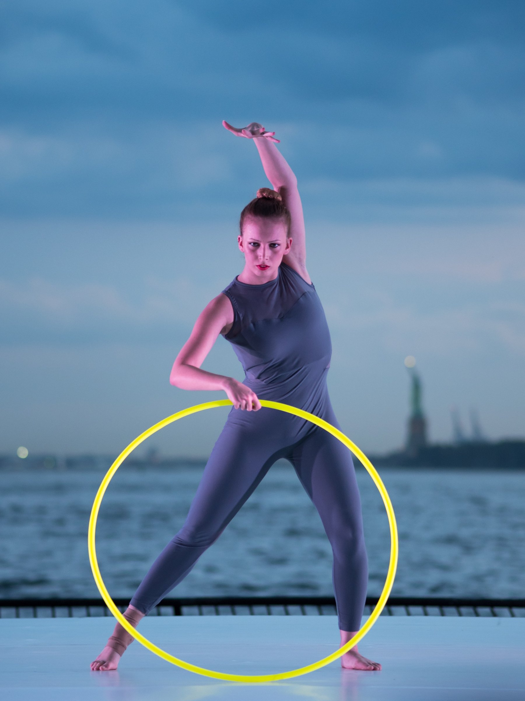 A dancer with a yellow hoop beneath a blue evening sky.