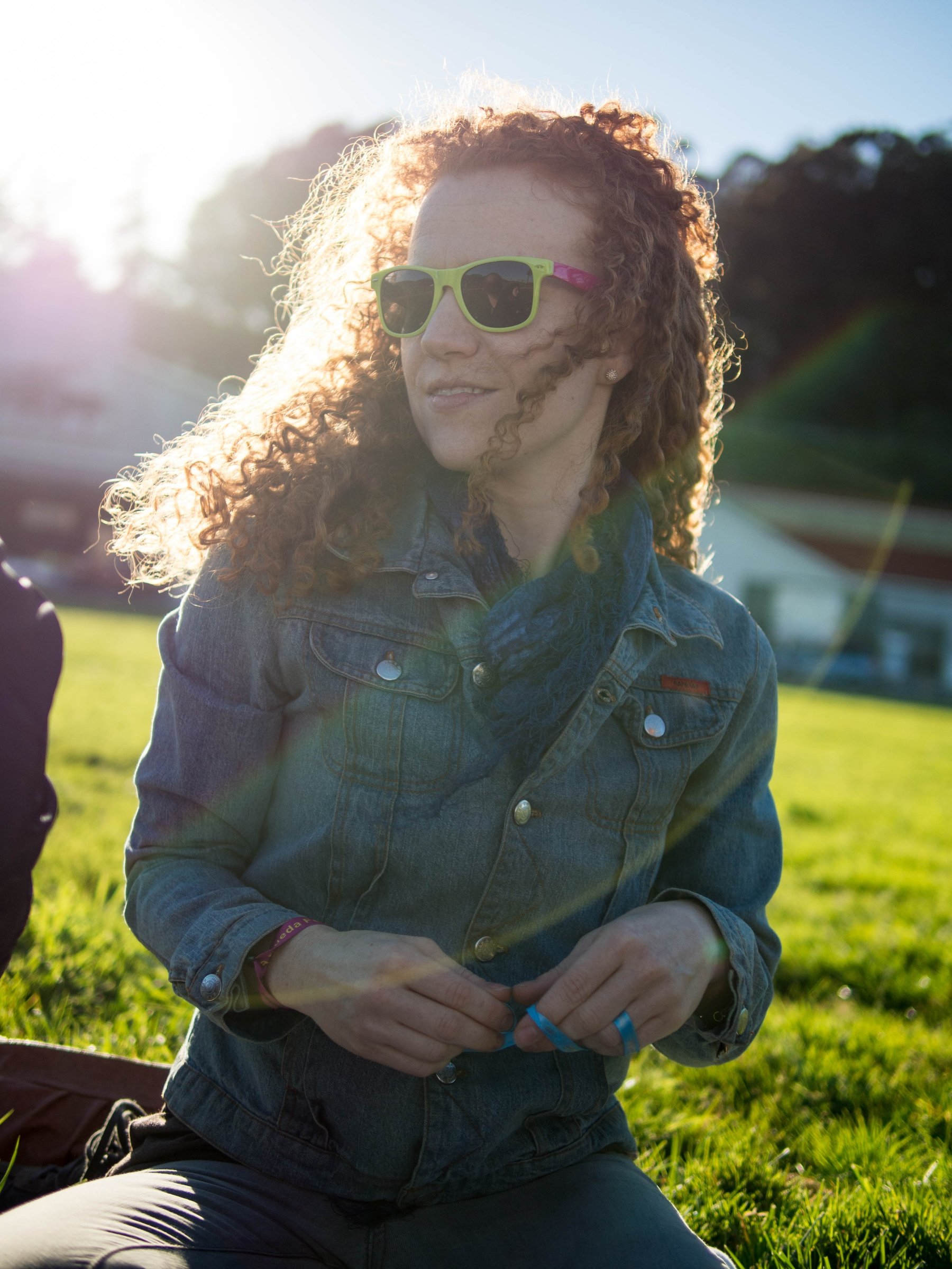 A woman in sunglasses sitting outdoors with sunlight shining through her hair.